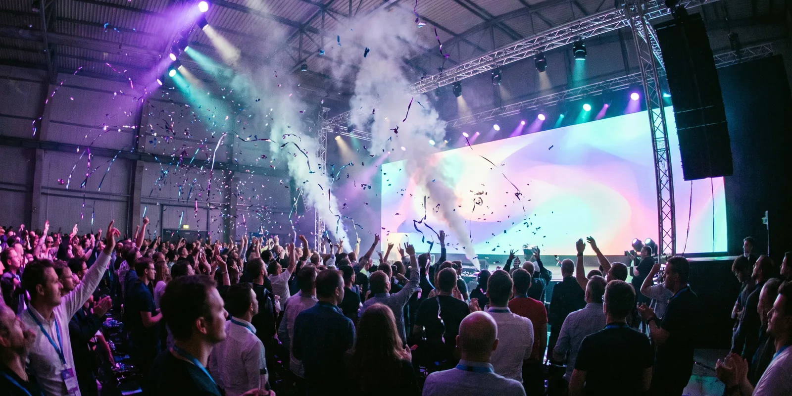 Confetti raining over a packed summit crowd in front of a glowing stage.