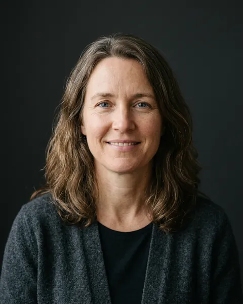 AI-generated portrait of Alice, a middle-aged white woman with shoulder-length wavy hair and a dark cardigan, smiling softly against a dark grey backdrop.