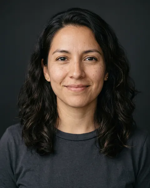 AI-generated portrait of Jessica, a young Latina woman with dark wavy shoulder-length hair and a charcoal t-shirt, smiling softly against a dark grey backdrop.