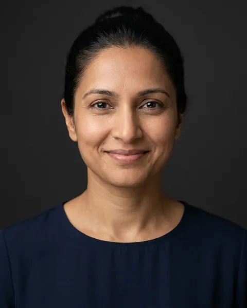 AI-generated portrait of Matilda, a middle-aged South Asian woman with dark hair pulled back and a dark blouse, smiling softly against a dark grey backdrop.